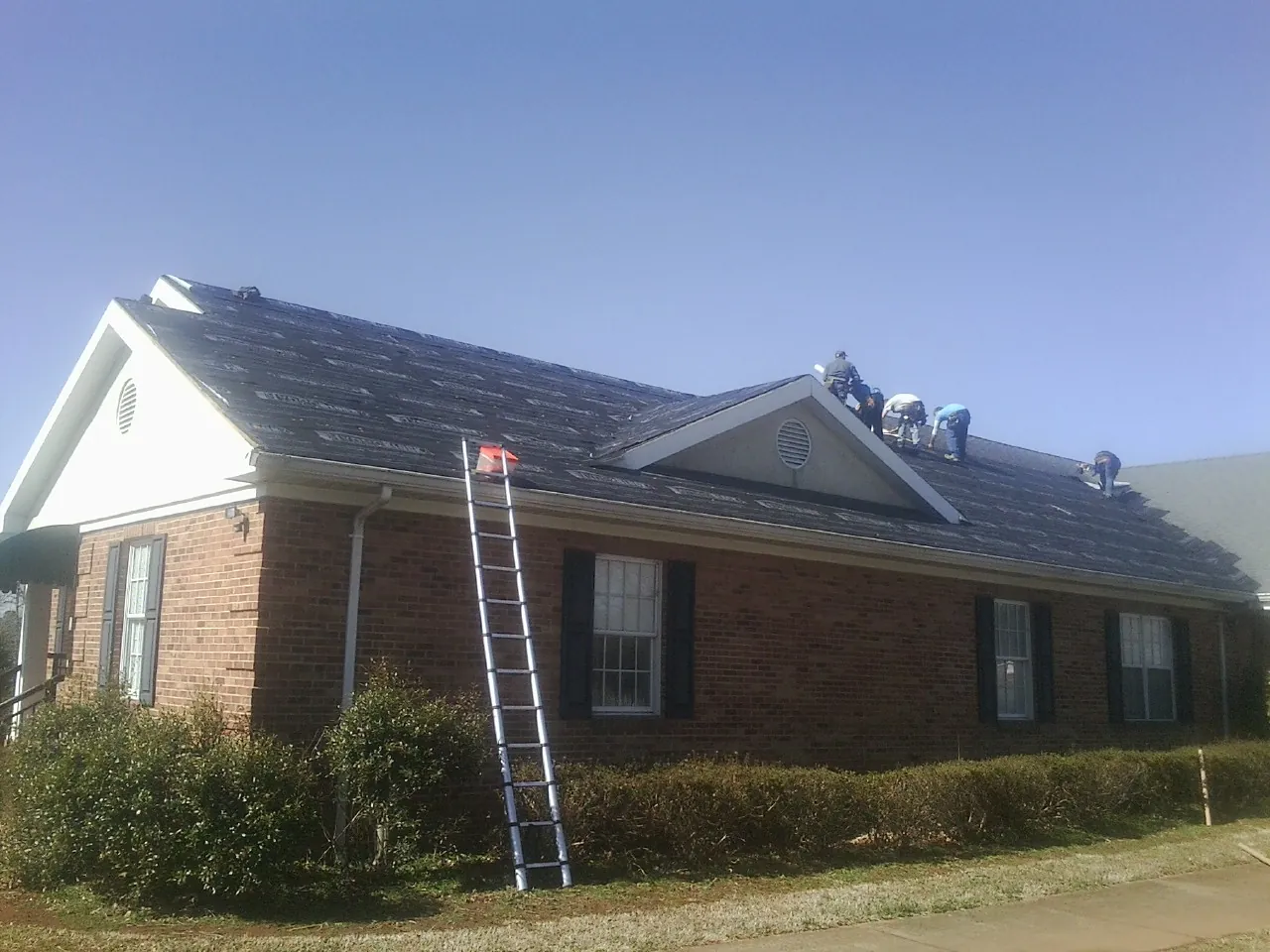 Crew tearing shingles off a brick ranch roof with a ladder set — Emergency Roof Repair work by our crew in Wales