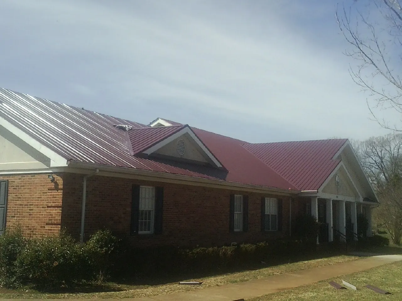 Red metal roof with gabled entries on a long brick building, from a Hail Damage Roof Repair job in Wales