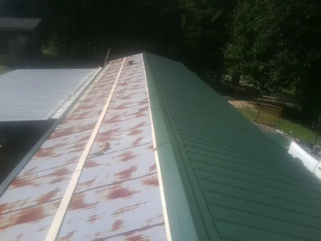 Old rusted panels beside newly installed green metal roofing — Wind Damage Roof Repair by Roofing Brothers in Wales