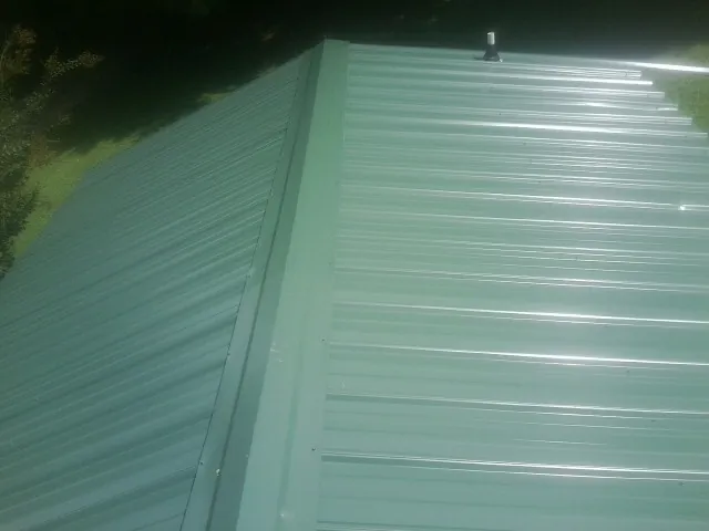 New green metal panels meeting at the ridge of a roof — Flat Roof Repair work by our crew in Wales