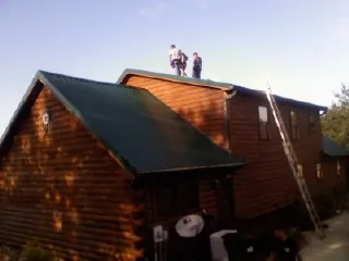 Crew on the ridge of a green metal roof on a two story log home in Wales