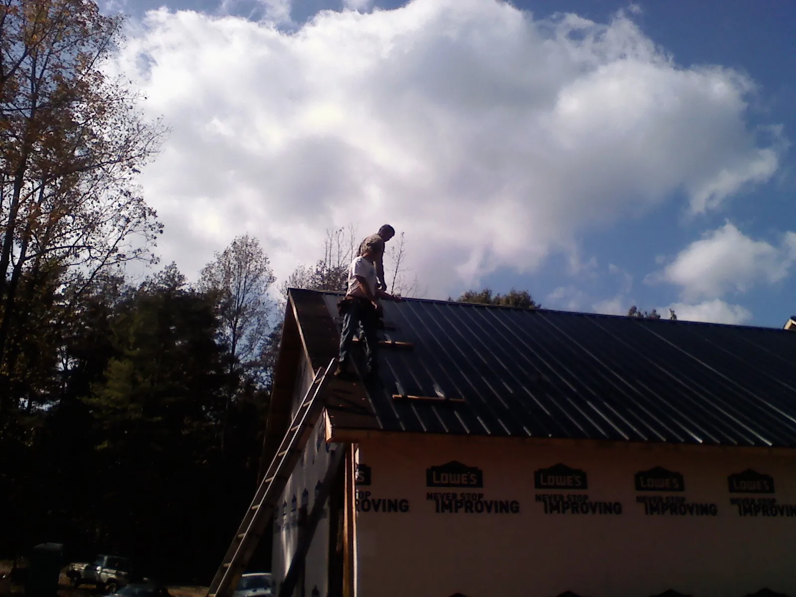 Roofer fastening dark metal panels high against a cloudy sky, from a Roof Inspection job in Wales