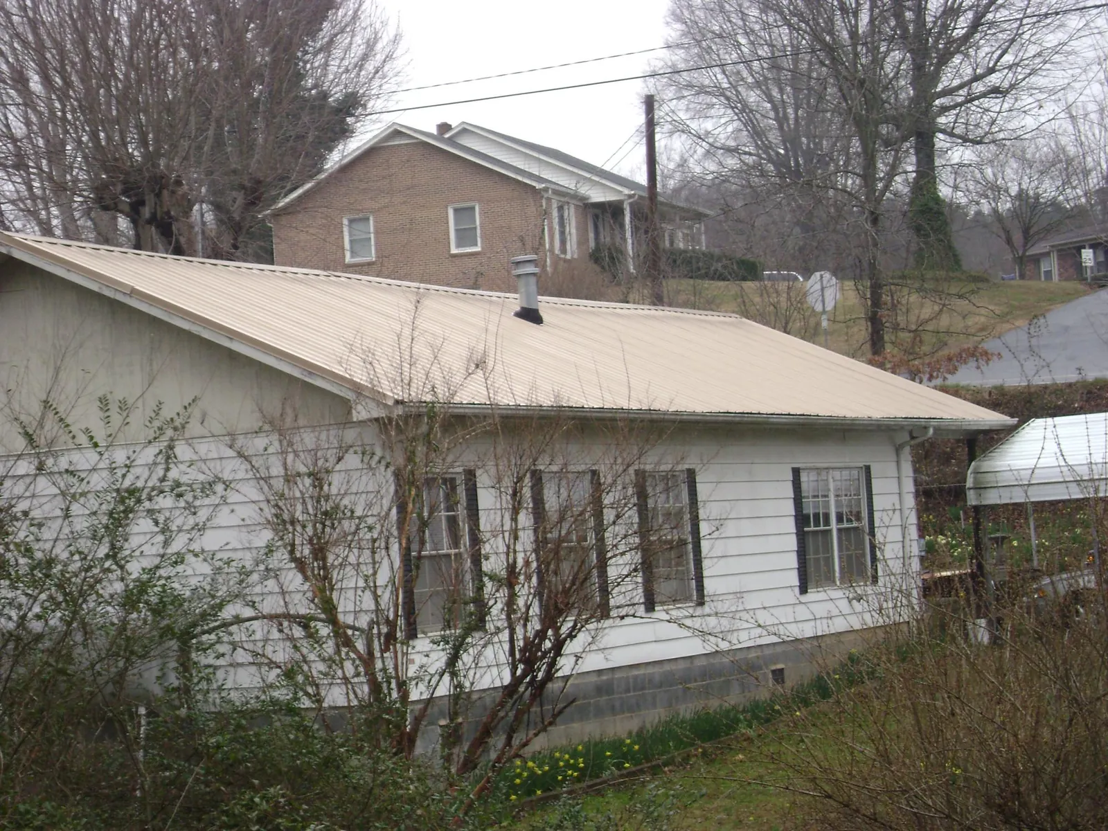 Tan metal roof on a white sided house set into a hillside — Commercial Roofing by Roofing Brothers in Wales