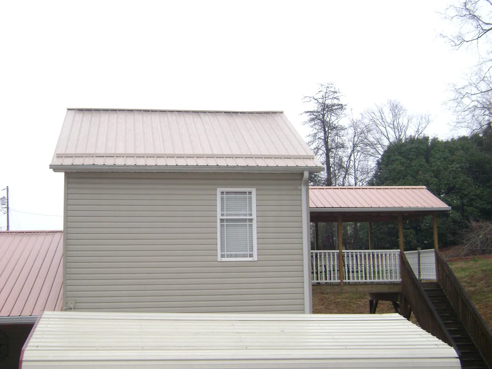 Tan metal roofs on a two story addition and attached porch, from a Roof Replacement job in Wales