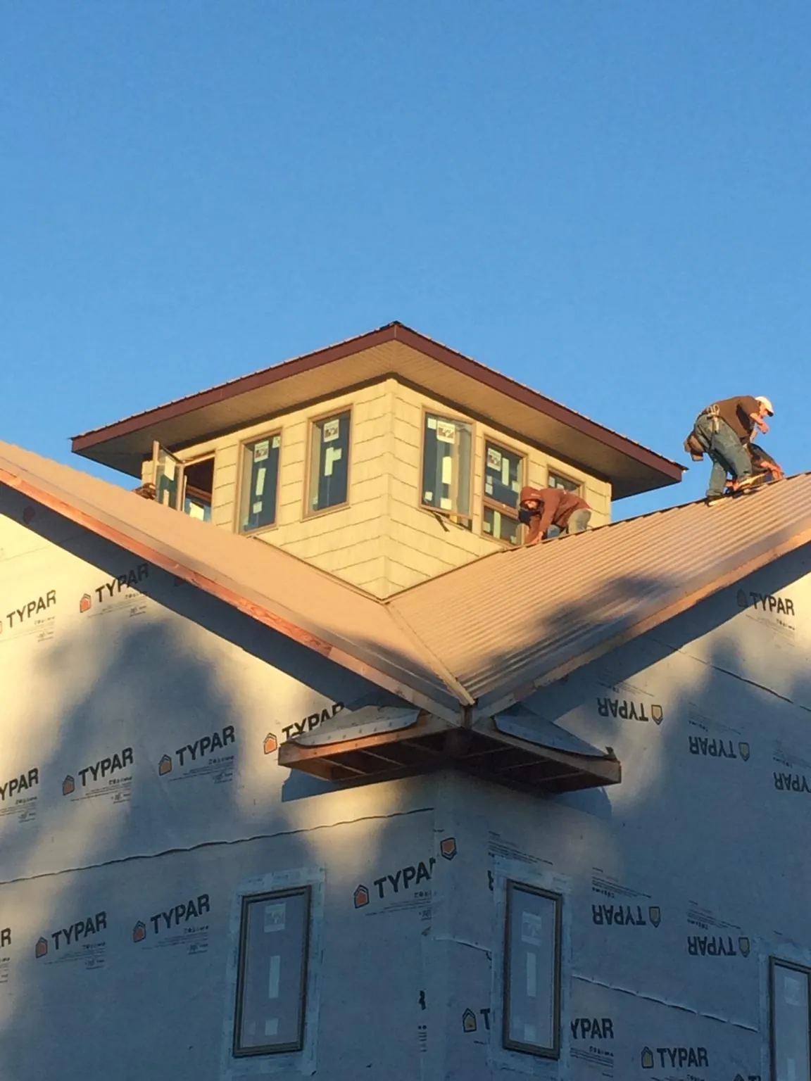 Roofers working around a rooftop cupola on a new metal roof at sunset — Roof Waterproofing in Wales by Roofing Brothers